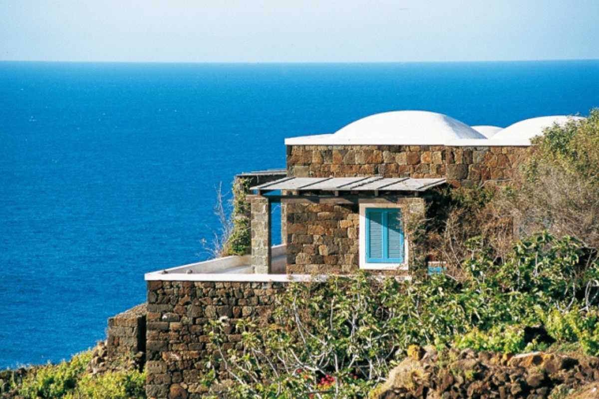 Vista panoramica della costa di Pantelleria con il mare blu, una strada che si snoda tra i capperi e i dammusi, atmosfera rilassata e assolata